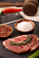 Raw pork meat steak with vegetables, peppers, tomato, salt, rosemary and spices cooking over stone table. Top view.