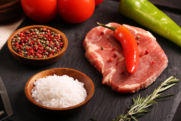 Raw pork meat steak with vegetables, peppers, tomato, salt, rosemary and spices cooking over stone table. Top view.