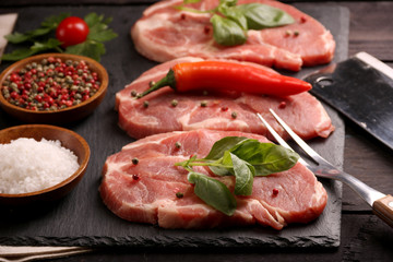 Raw pork meat steak with vegetables, peppers, tomato, salt, rosemary and spices cooking over stone table. Top view.