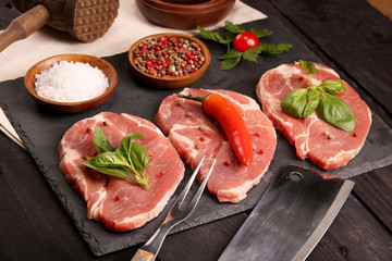 Raw pork meat steak with vegetables, peppers, tomato, salt, rosemary and spices cooking over stone table. Top view.
