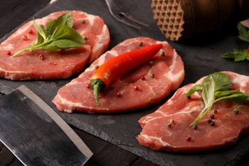 Raw pork meat steak with vegetables, peppers, tomato, salt, rosemary and spices cooking over stone table. Top view.