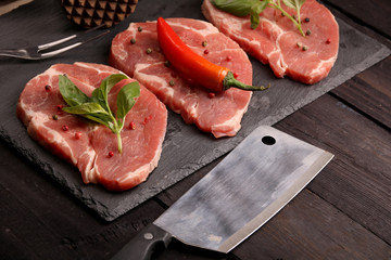 Raw pork meat steak with vegetables, peppers, tomato, salt, rosemary and spices cooking over stone table. Top view.