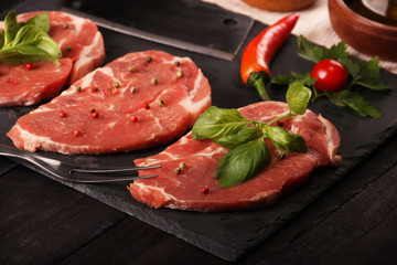 Raw pork meat steak with vegetables, peppers, tomato, salt, rosemary and spices cooking over stone table. Top view.
