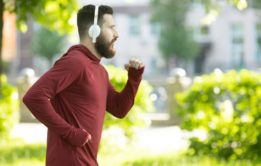Obraz premium Fit bearded young man jogging through a park listening to music on his mobile phone.