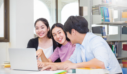 Portrait of asian university students man woman discussing reading books with computer together in the library campus. Education tutor exam group study brainstorm teamwork success people concept