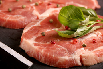 Raw pork meat steak with vegetables, peppers, tomato, salt, rosemary and spices cooking over stone table. Top view.