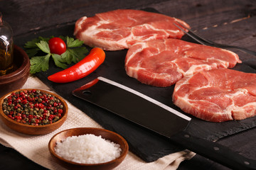 Raw pork meat steak with vegetables, peppers, tomato, salt, rosemary and spices cooking over stone table. Top view.