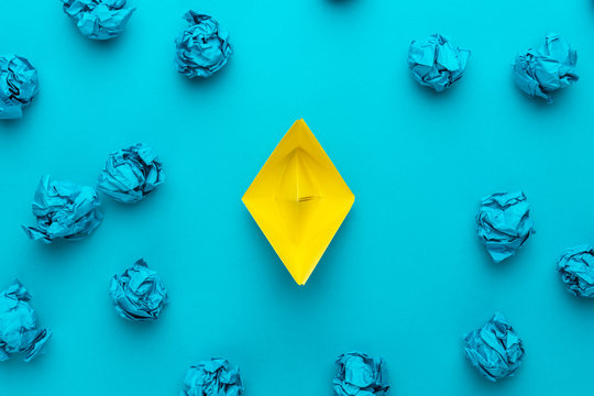 new idea concept with crumpled office paper and yellow paper ship. top view of great business idea concept over blue background with yellow paper boat in the center