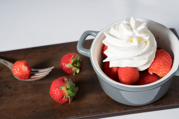 fresh strawberries with whipped cream  in grey bowl,  with fork and wooden plate