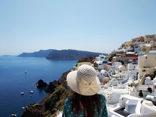 Obraz premium Beautiful young woman in green dotted dress walking in Oia, Santorini streets. White houses, blue sea