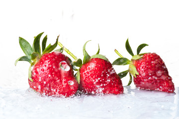 Several ripe wet red strawberries on white or colored background with splashes of water