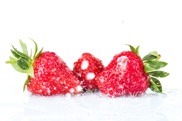Several ripe wet red strawberries on white or colored background with splashes of water