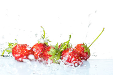 Several ripe wet red strawberries on white or colored background with splashes of water