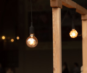 Vintage filament lamp with coil shape light hanging from the ceiling of dark background.