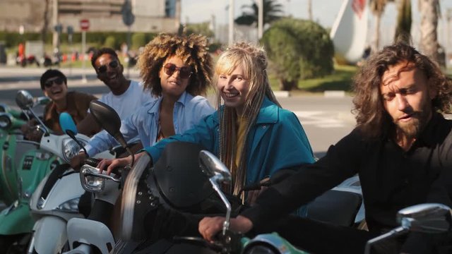Trendy young friends on scooters waving at camera