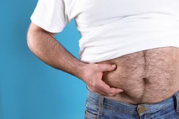 Overweight man with large belly on color background, closeup