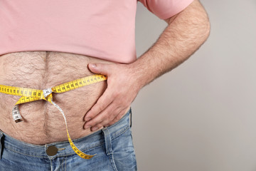 Overweight man with large belly and measuring tape on color background, closeup