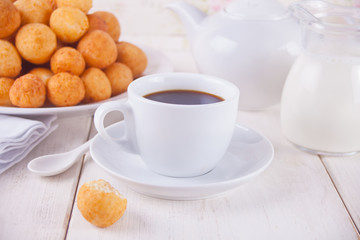 Obraz na płótnie Canvas Cup of coffee with small balls of freshly baked homemade cottage cheese doughnuts in a plate on a background.