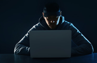 Man using laptop at table on dark background. Criminal activity