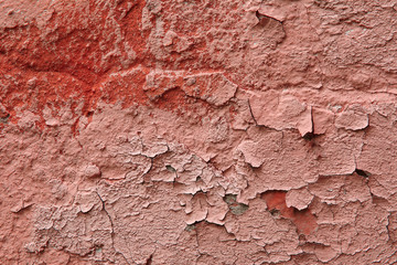 Fragment of an old exterior wall with cracked peeling plaster pink color