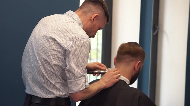 Close up shot of man getting trendy haircut at barber shop. Male hairstylist serving client, making haircut using machine and comb