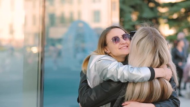 Girls reunion. Young female best friends happy to meet, hugging on city street. Defocused background.