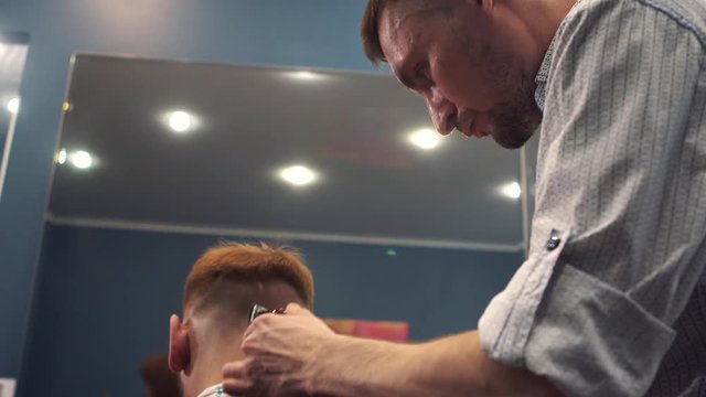 Close up shot of man getting trendy haircut at barber shop. Male hairstylist serving client, making haircut using machine and comb