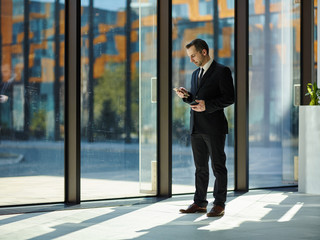 Full length portrait of busy multi-tasking middle aged businessman in black suit standing near...