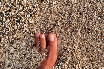 Top view of man standing bare feet on beach. Texture of bottom, leg and foot of man drowning with sweeping colorful stone below on rocky stones beach in sea with waves and foam, water ripples of sea.