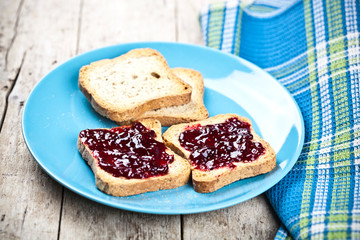 Fresh toasted cereal bread slices with homemade wild berries jam and linen napkin on blue ceramic plate closeup on rustic wooden background. Sweet food for breakfast with.