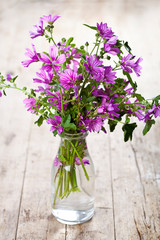 Fototapeta na wymiar Wild violet flowers in glass bottle on rustic wooden table.