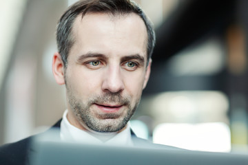 Close-up of handsome middle aged businessman with stubble reading information on laptop screen