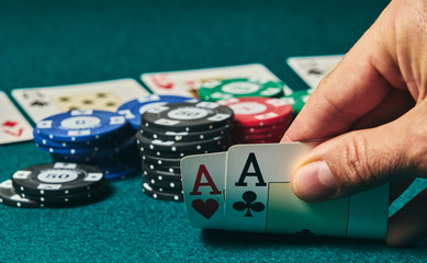 close-up of two aces held in one hand on the green game mat on the right side of the image to leave room for editing, other cards and poker chips are on the mat