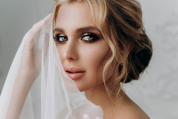 Bride with a beautiful hairstyle. Model blonde in a wedding dress in white interior