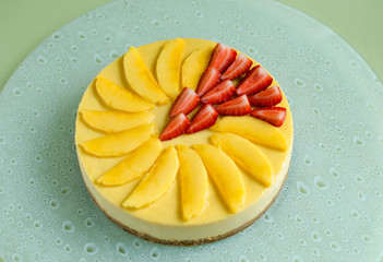 Mango cheesecake decorated with fresh strawberry on glass plate on green background