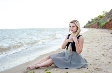 Fototapeta na wymiar girl sitting on the beach in cloudy weather, in a dress 
