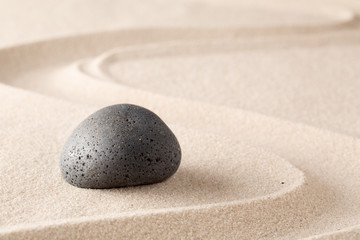 Black basalt stone on sandy beach sand with line pattern. Spa wellness or zen meditation garden background. .