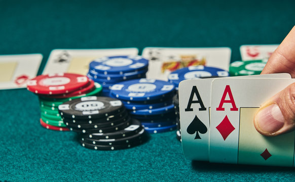 close-up of two aces held in one hand on the green game mat on the right side of the image to leave room for editing, other cards and poker chips are on the mat
