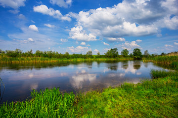 beautiful summer river scene with cumulus clouds reflected in a water