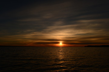 Sunset sun circle in the haze of a cloudy sky above the water surface of the lake