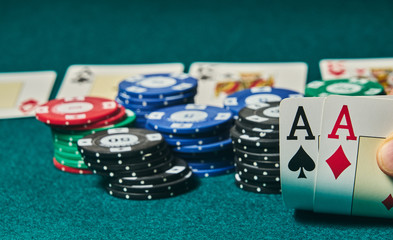 close-up of two aces held in one hand on the green game mat on the right side of the image to leave room for editing, other cards and poker chips are on the mat