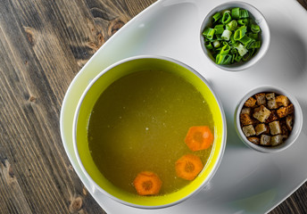 Chicken soup with green onion and croutons in bowl on wooden table