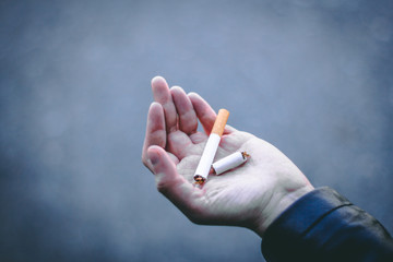 Young person’s hand holding a cigarette that is broken in two – Toxic an un healthy habit that can cause cancer and other diseases – Concept image for quit smoking and no smoking day
