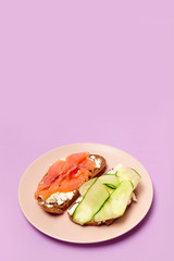 Morning breakfast of assorted sandwiches with various fillings: with fish, cheese and cucumber on a purple background.