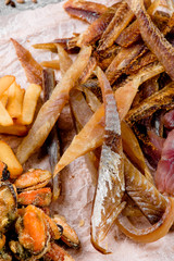 Beer Snack. Dried fish close upAssorted beer snacks: fried mussels, dried fish, french fries, cheese sticks on kraft paper on a tray on a concrete background in a beautiful composition with vegetables