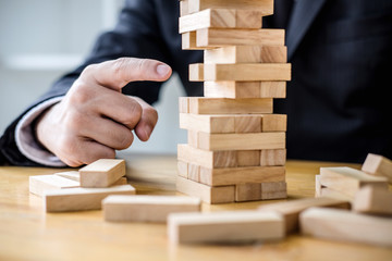 Alternative risk plan and strategy to growth profit in business, Young intelligent businessman playing the wood game, hands of executive placing wood block on the tower