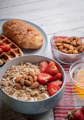 Breakfast set. Traditional muesli or oatmeal porridge on white background. With delicious food - berry, belgian waffle, almond, croissant and honey