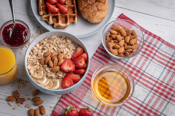 Traditional breakfast on white table. Sweet oatmeal with berry, delicious belgian waffle. Muesli. Dessert. Morning meal. Organic food. Honey, almond, jam, orange juice, croissant. Top view