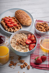 Breakfast table with oatmeal, waffles and croissant, fresh homemade belgian wafer and orange juice