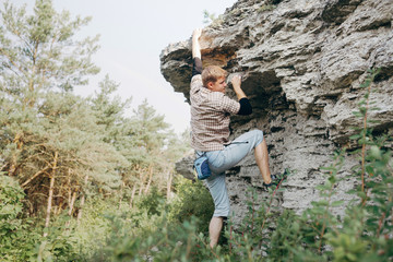 Naklejka na ściany i meble Brave young man climbs the cliff